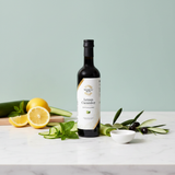 Tastefully Olive Lemon Cucumber white balsamic bottle with lemon slices, cucumber ribbons, mint, and a white bowl.