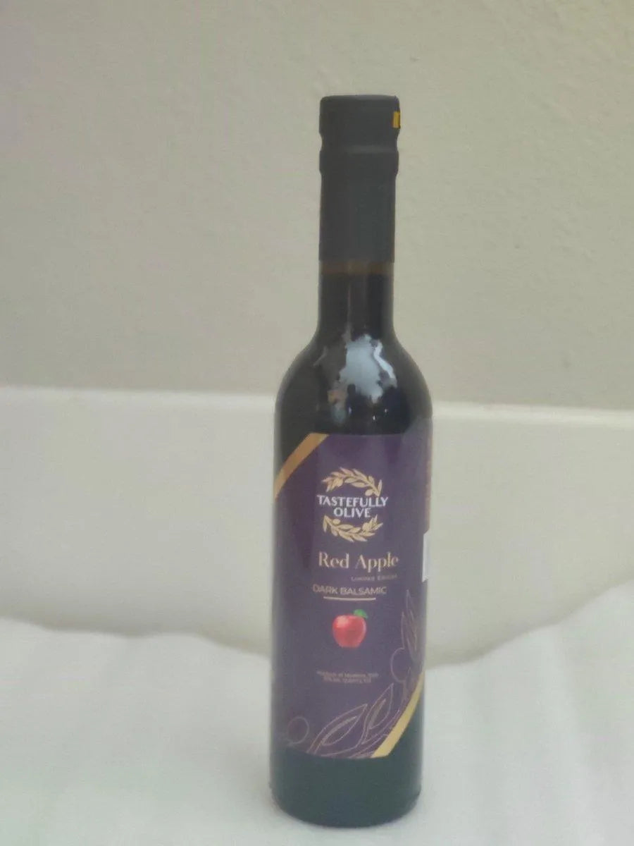 Tastefully Olive Red Apple dark balsamic bottle with a purple label and black cap against a pale background.