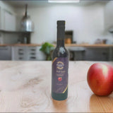 Tastefully Olive Red Apple dark balsamic bottle beside a red apple on a wooden kitchen counter.